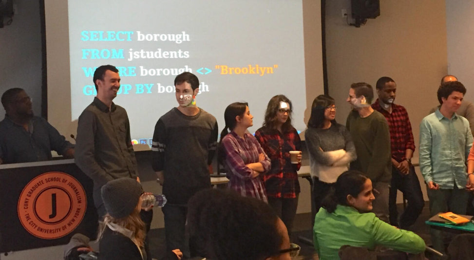 Photo of grad students standing before projection screen, participating in fun, human query result exercise.