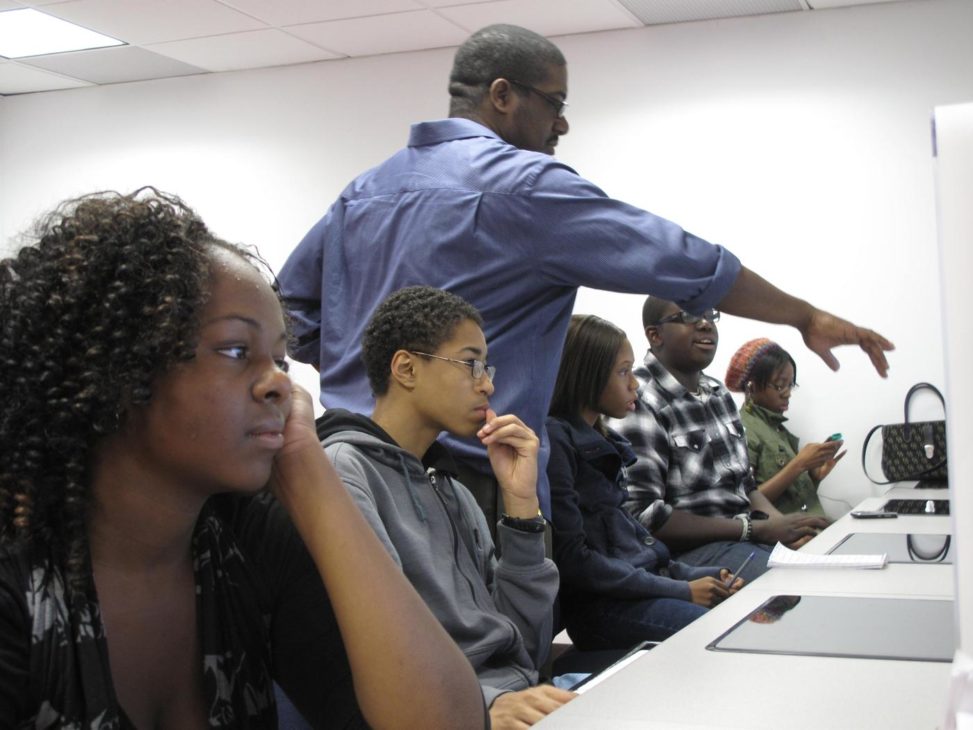 Photo of me standing over the shoulders of teen students, pointing at information on one of their computer screens.